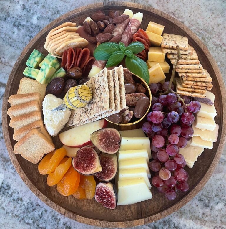 beautifully displayed meat and cheese platter with fruit and colors spread across a circular wooden board